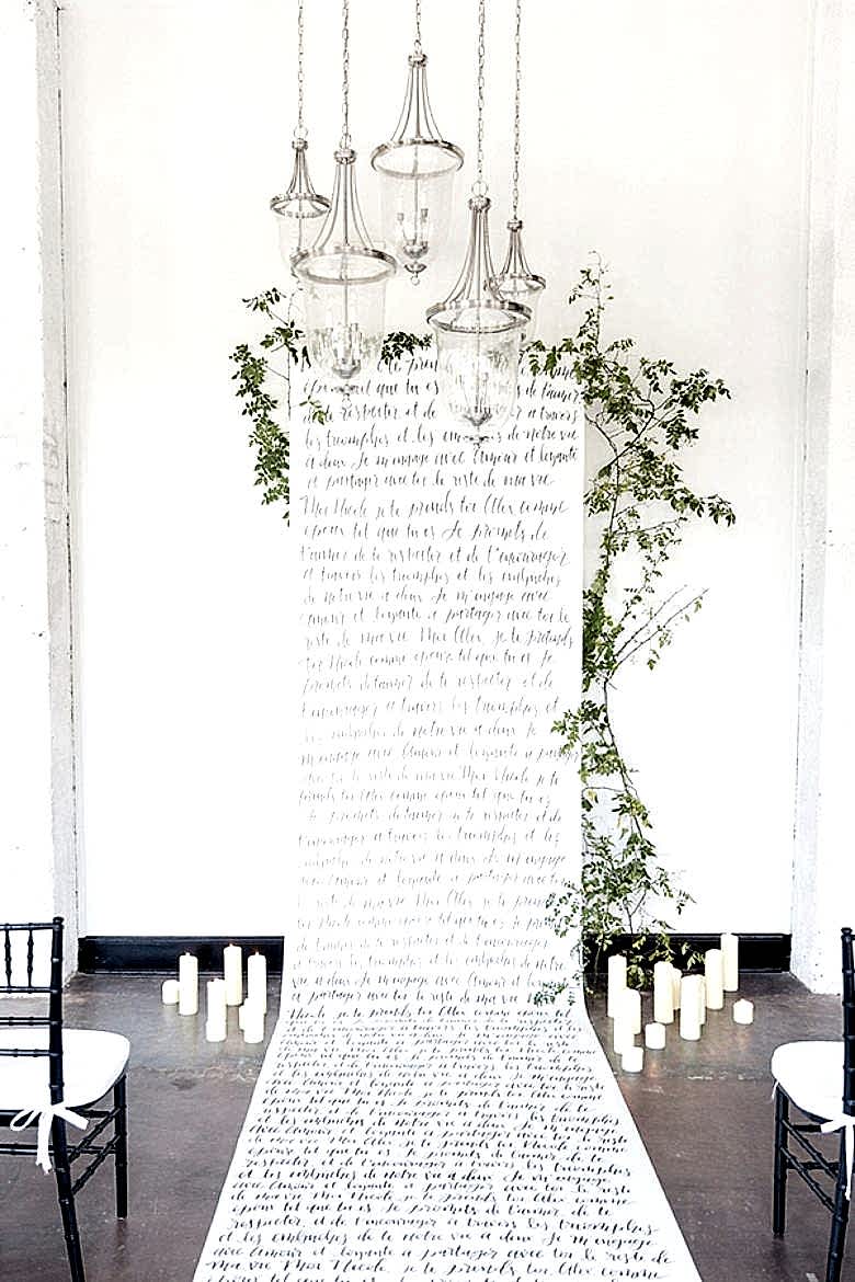 long handwritten-style scroll as backdrop to altar as well as aisle, bordered by white pillar candles on the ground and clear glass pendant lights handing above