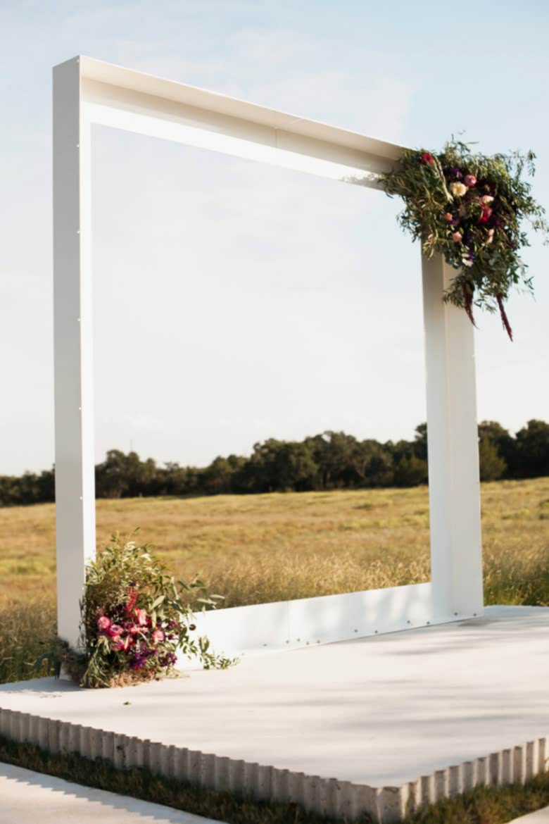 large white square frame on a short raised cement altar, adorned with flowers in two opposite corners, in a field