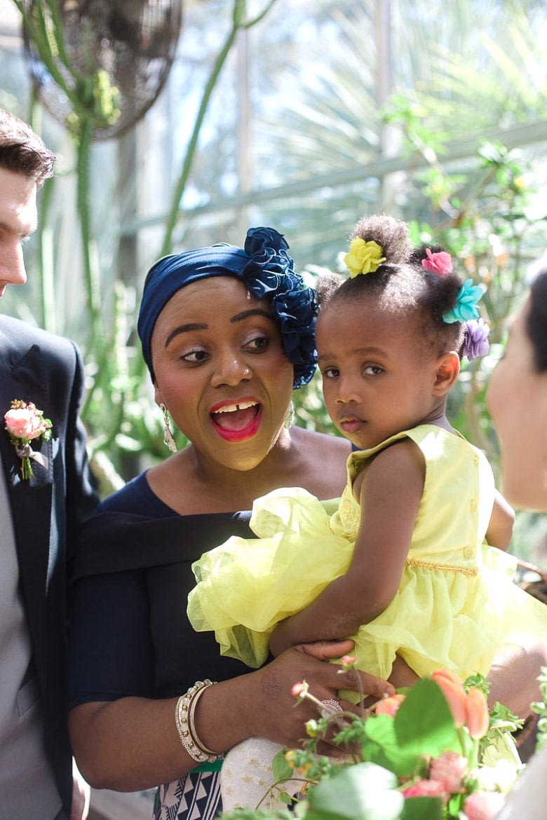 happy woman holding small girl in yellow dress in brightly lit greenhouse-style room in a Gina Clyne photo