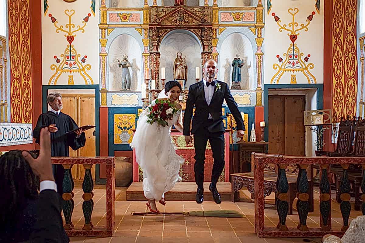 bride and groom jump over a broom at the altar of an ornately decorated chapel in a Gina Clyne photo