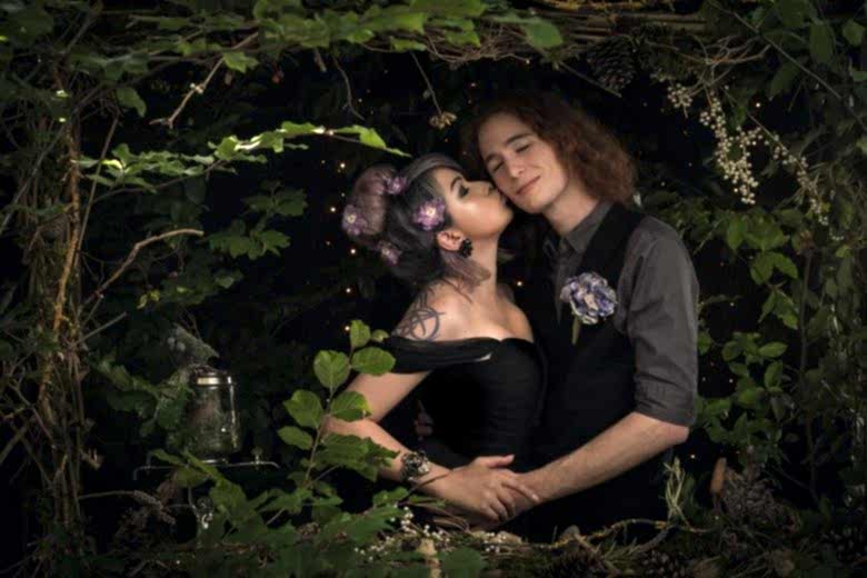 couple in black and grey wedding finery embrace in a dark room made to look like a forest with a dark starlit sky