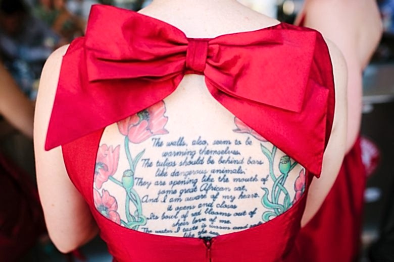 a woman's back full of tattoos seen through the window of a dress