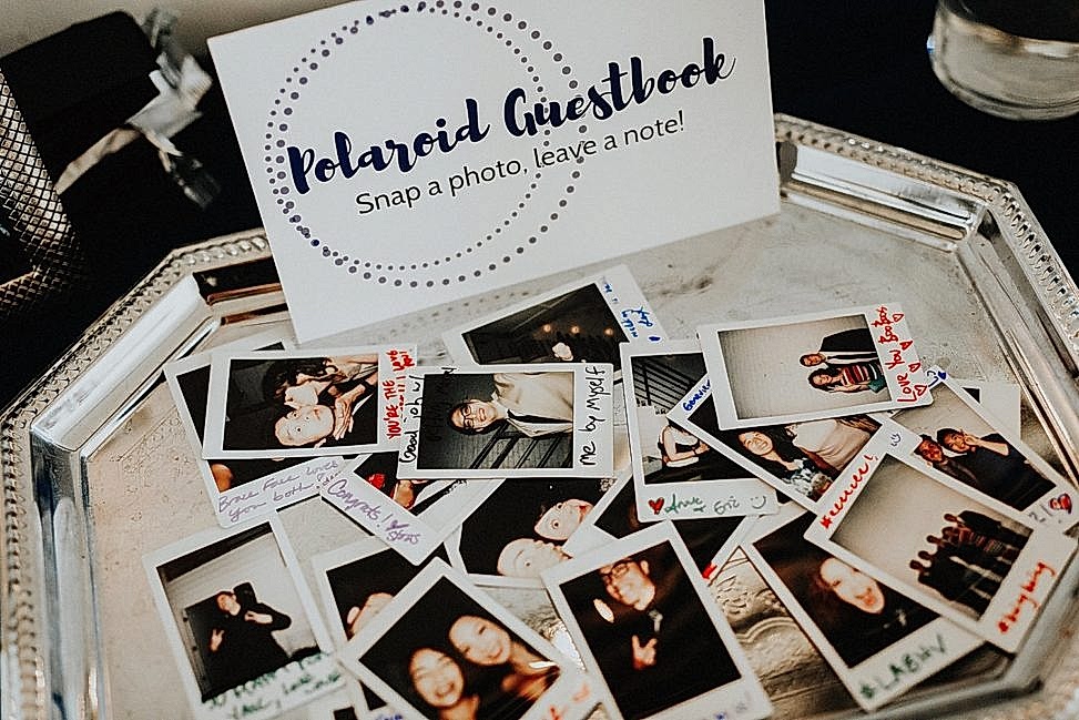 a pile of instax mini photos sits on a silver tray next to a sign that says "Polaroid Guestbook"