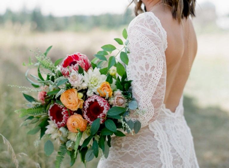 close up of a bride wearing a backless lace gown carrying a wild bridal bouquet with protea