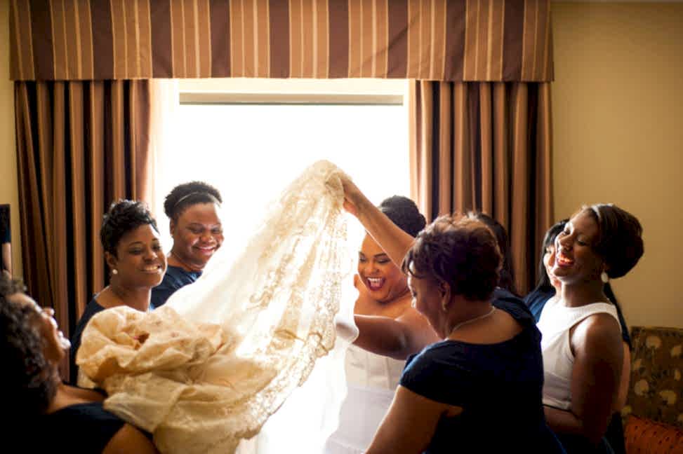 bride surrounded by bridesmaids helping her into dress in a photo by You Are Raven