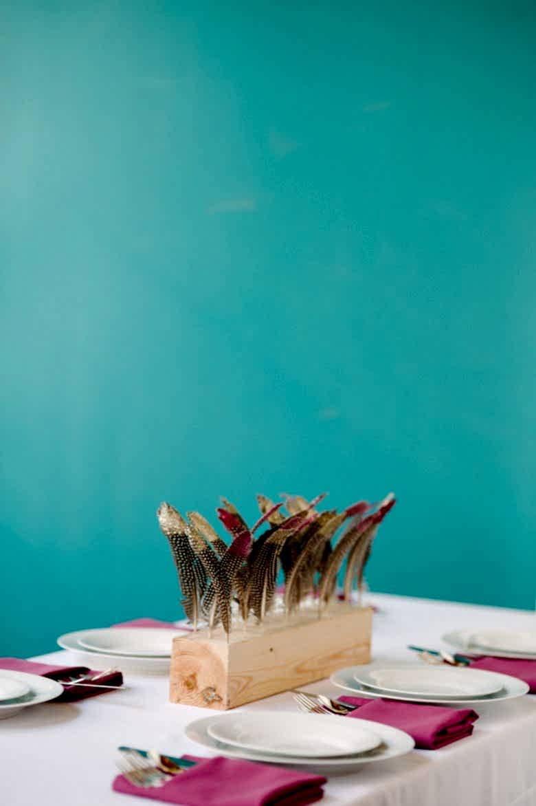 diy wood block wedding centerpiece with painted gold feathers and hot pink napkins in front of a teal wall