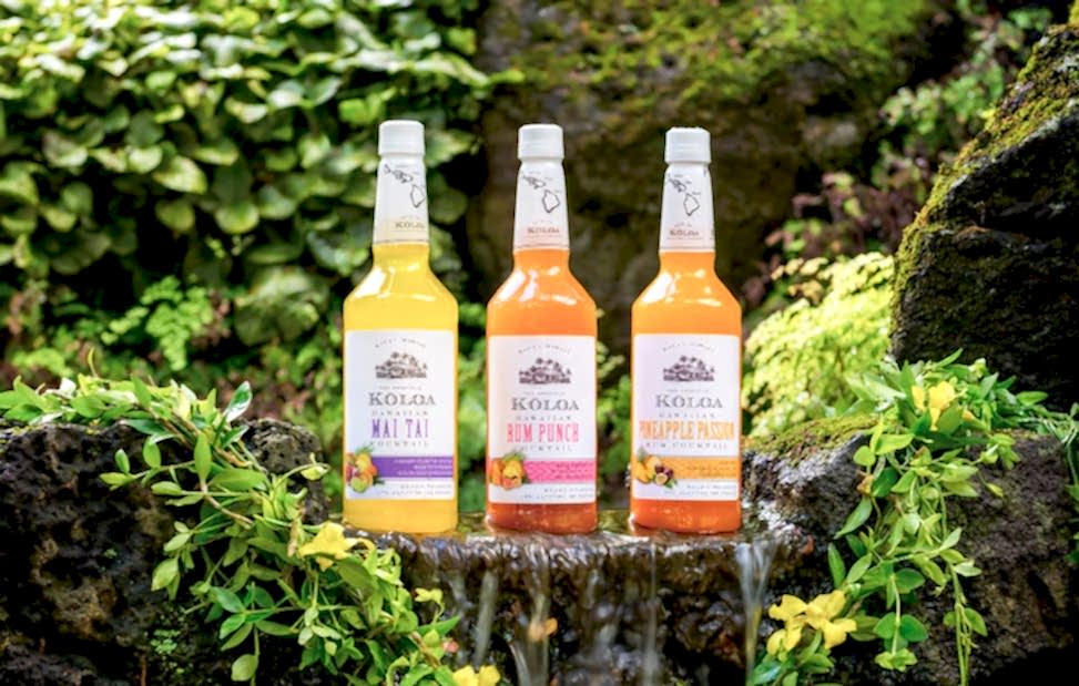 Trio of Koloa rum bottles sitting on rock among leaves