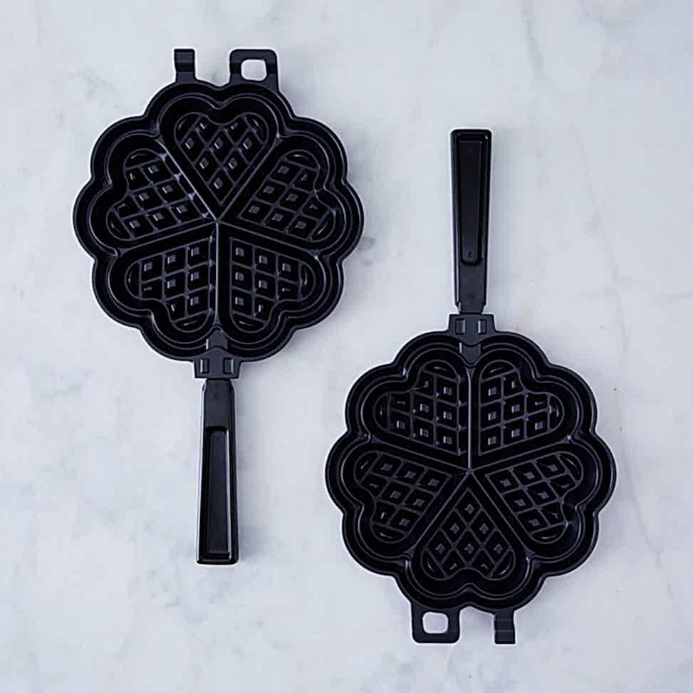 Two waffle irons with heart shapes on a marble table