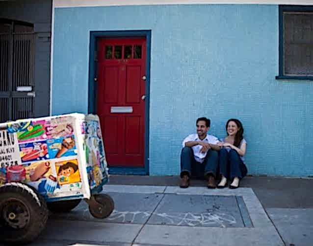 woman and her husband sitting in front of a light blue tiled wall next to an ice cream push cart