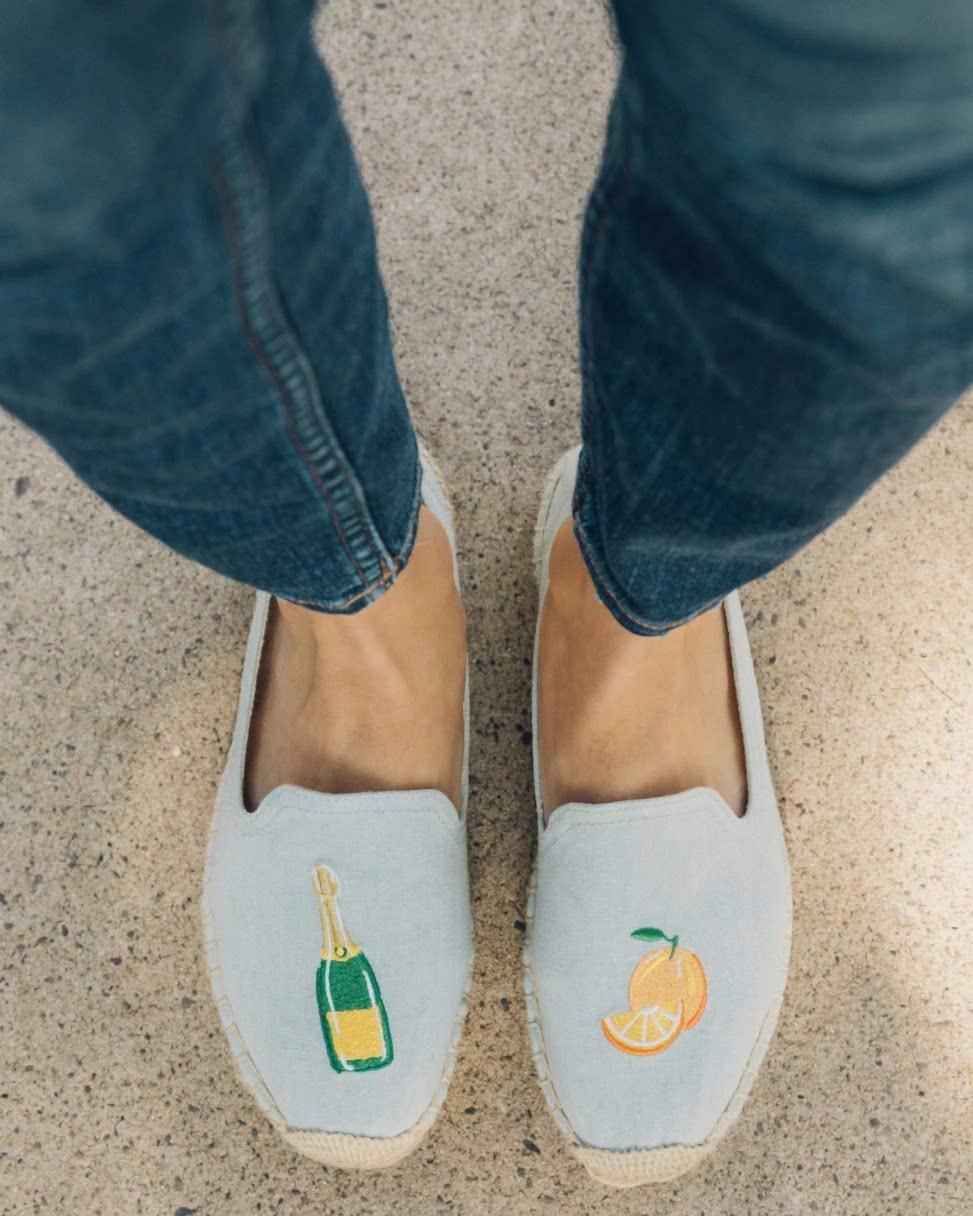 Blue slip-on shoes with a champagne bottle and orange embroidered design