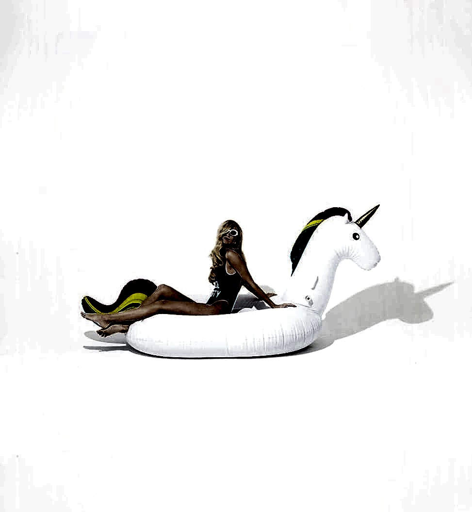 Blonde woman in swimsuit sitting in pool floaty of unicorn with rainbow hair
