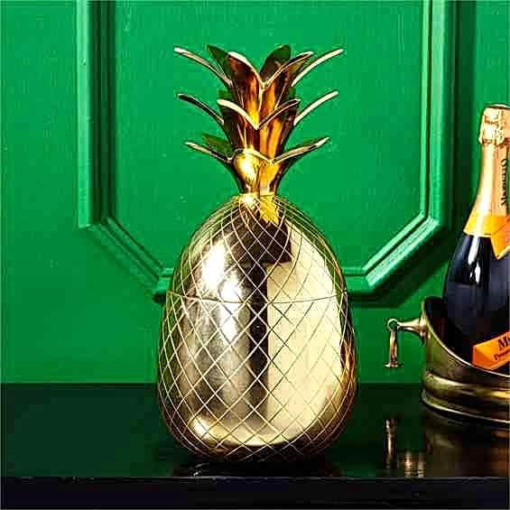 Pineapple shaped gold ice bucket with lid sitting on bar before green wall
