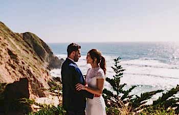 Couple looking into each other's eye on the beach with the sun high on the water