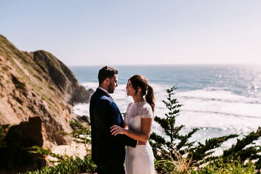 Couple looking into each other's eye on the beach with the sun high on the water