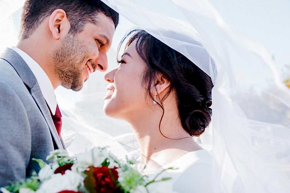 a woman and man underneath a veil, smiling
