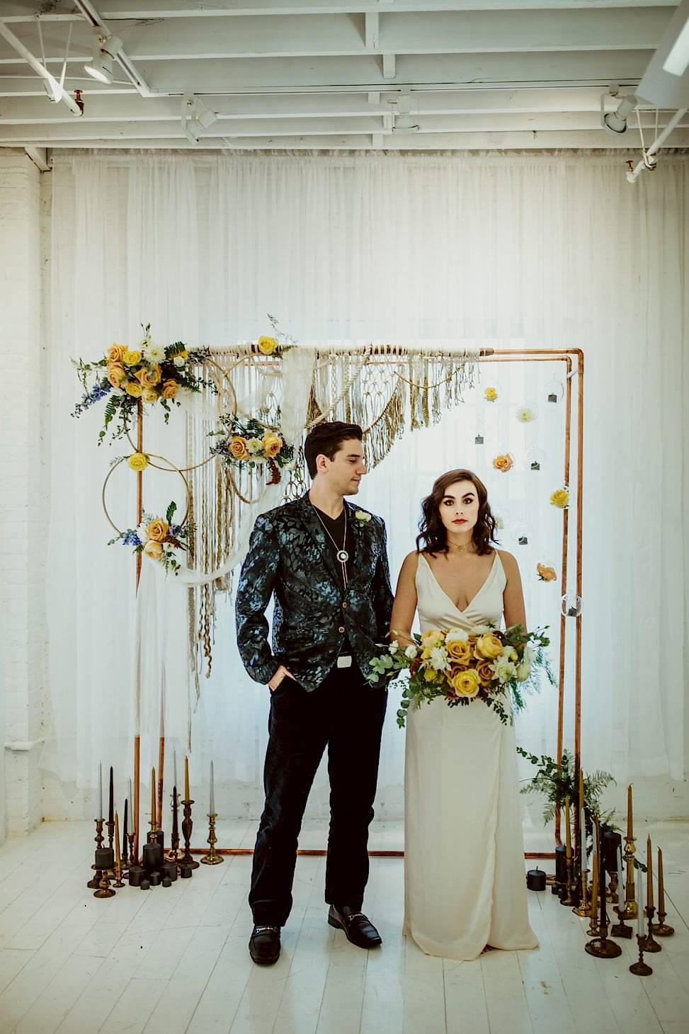 bride and groom standing near an alter with flowers, macrame, and candles