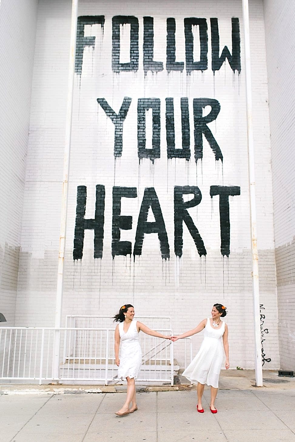 couple smiling in front of "Follow Your Heart" mural