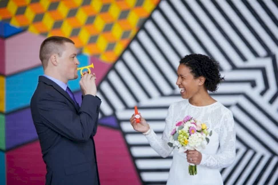 couple playing with kazoos and laughing in front of a mural