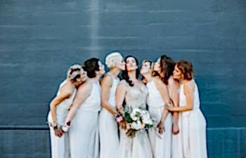 Bridesmaids in white kissing a bride