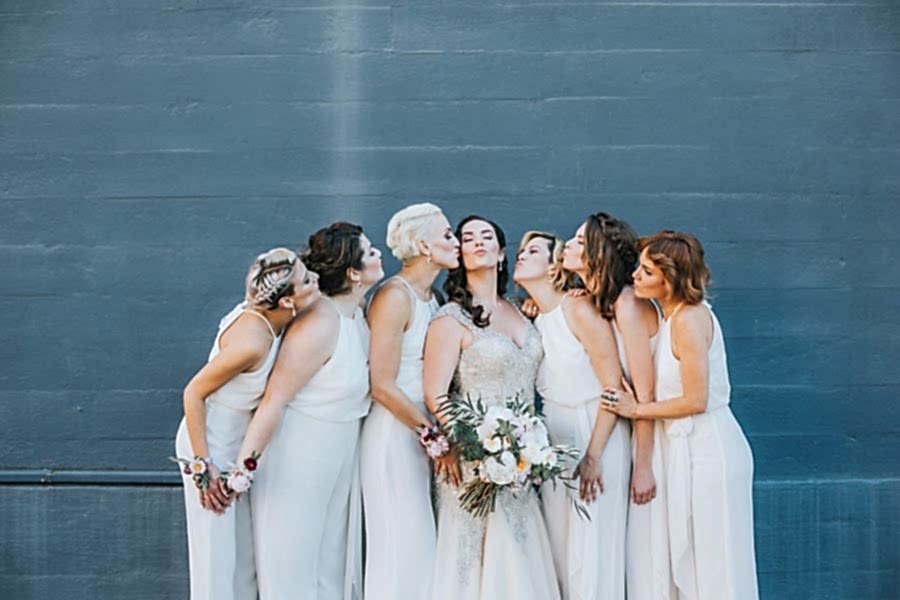 Bridesmaids in white kissing a bride