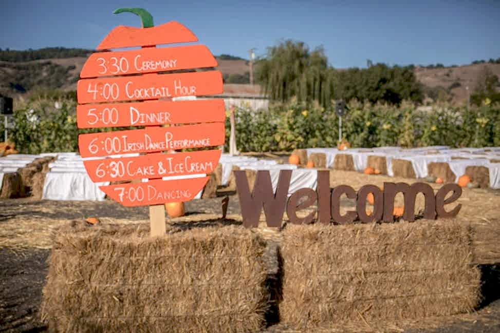 wedding order of events painted on a pumpkin shaped sign on a bale of hay