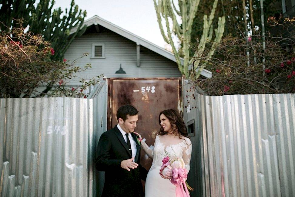 couple smiling and dancing in front of rusty metal gate and corrugated fence