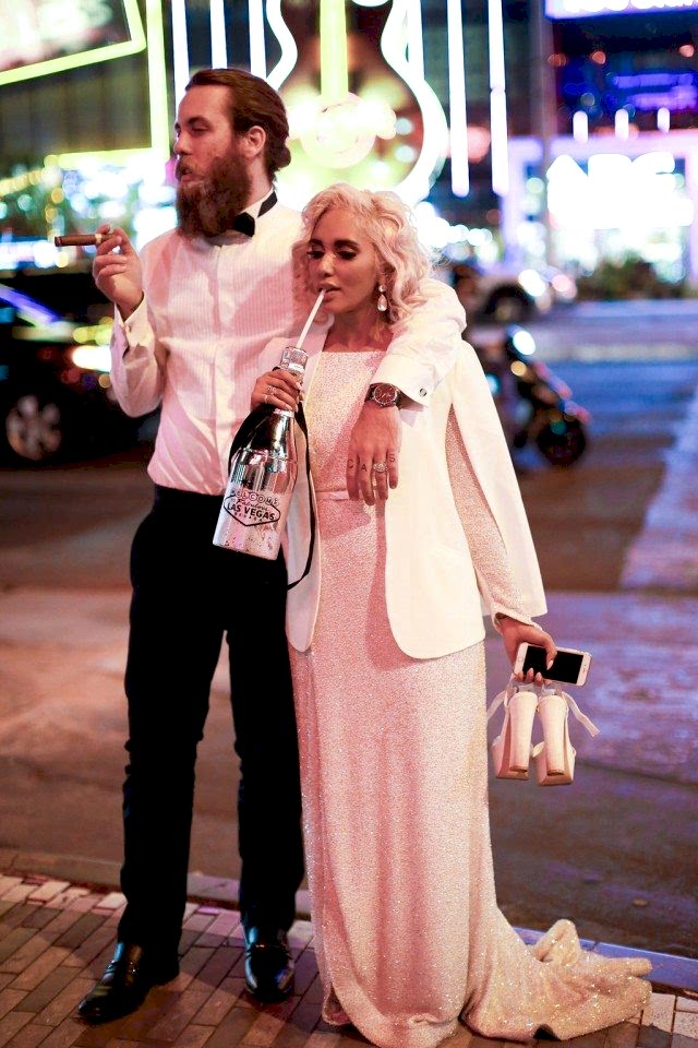 bride wearing a sequin gown drinking out of a champagne bottle holding her shoes while groom smokes a cigar