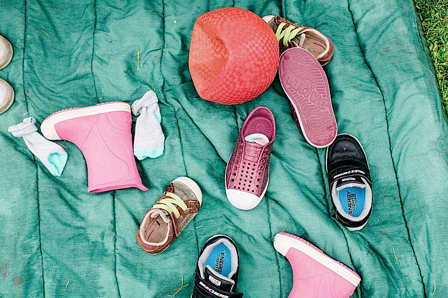 Several different sizes and styles of children's shoes strewn over a blanket outside