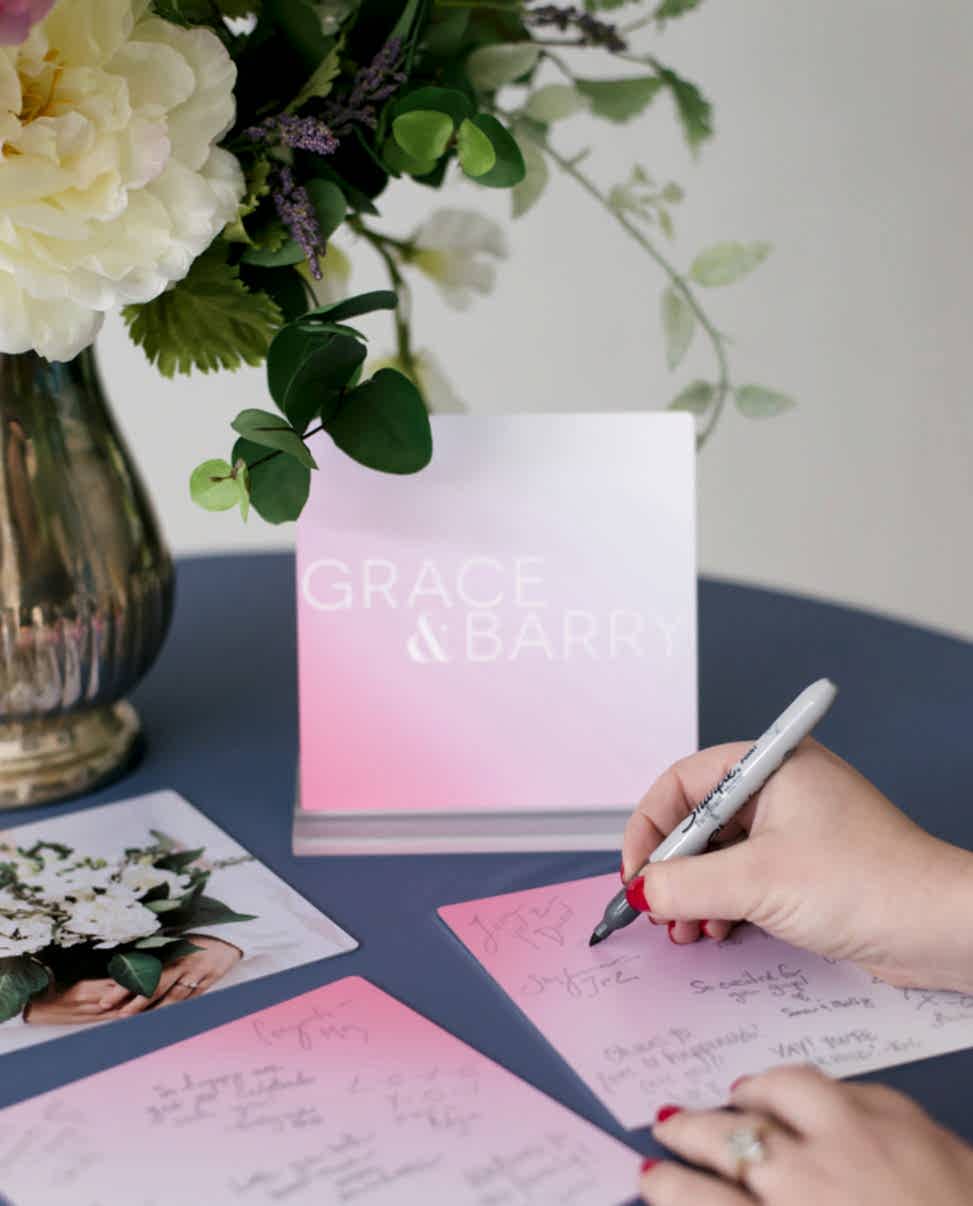 a flower arrangement next to metal prints that a woman is signing