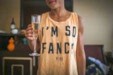 Woman holds glass of champagne while wearing a shirt that reads I'm So Fancy