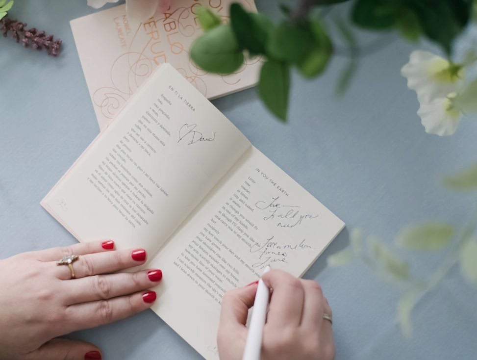 woman's hands signing a poem book on a blue tablecloth