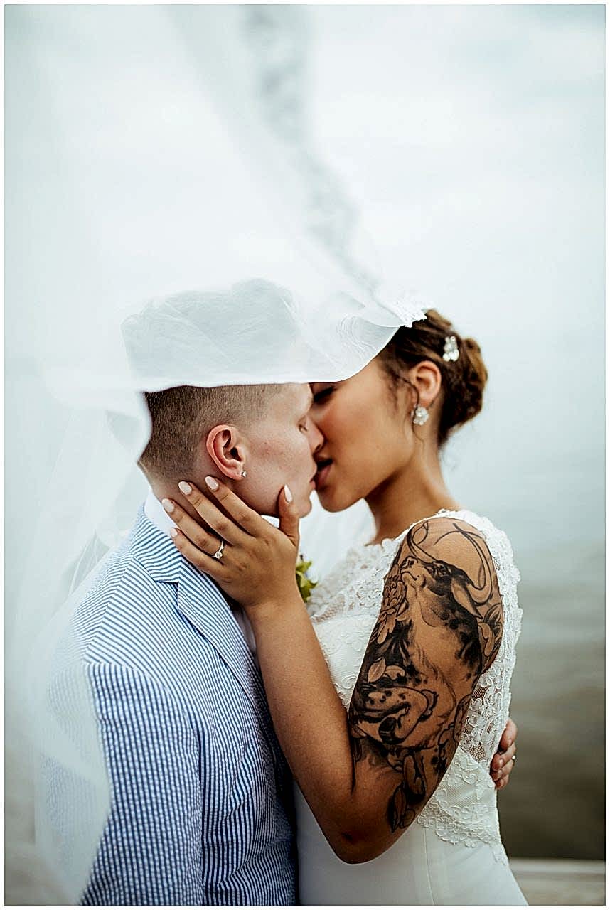 A wedding couple kiss as the wedding veil blows in the wind