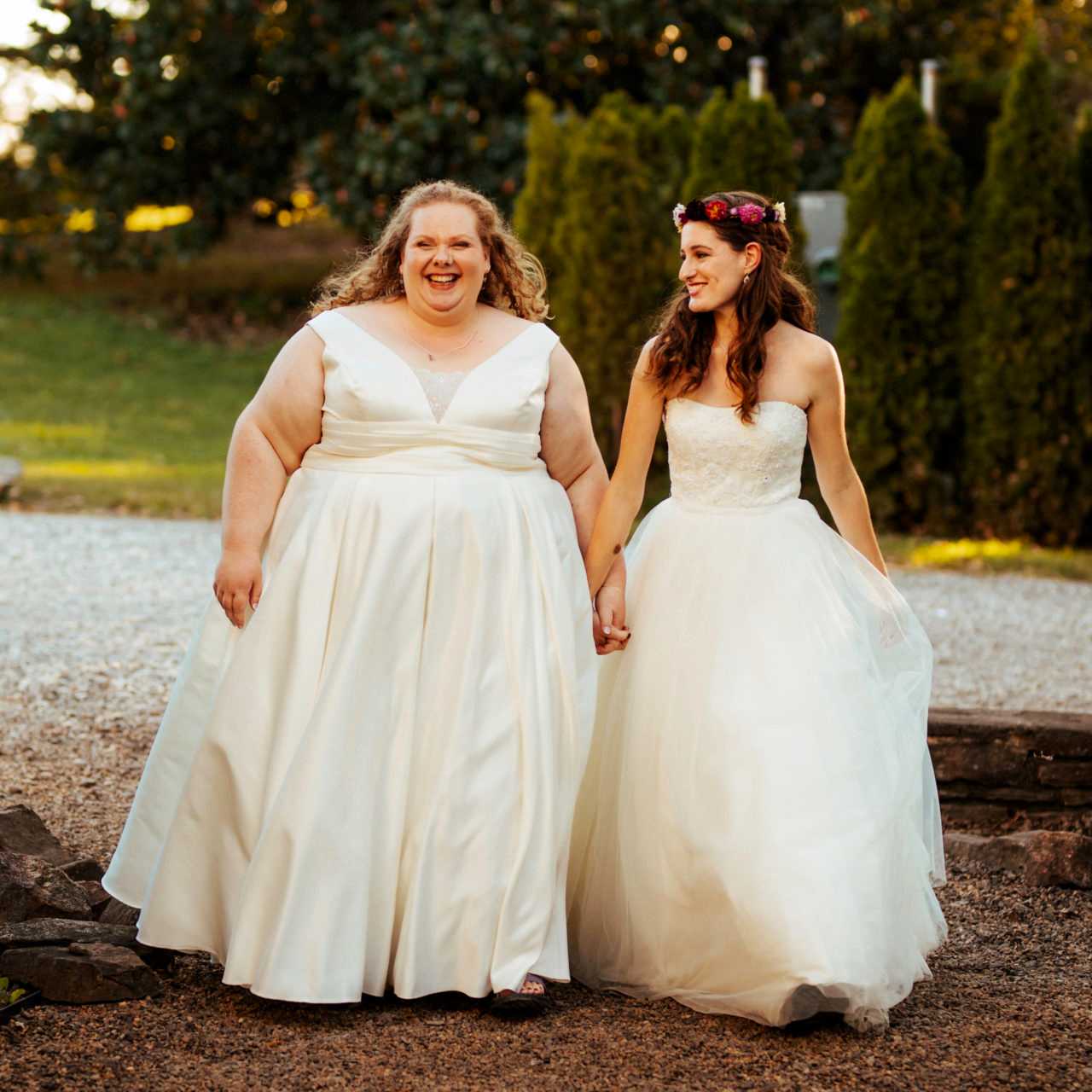 Two women in wedding dresses hold hands and walk together