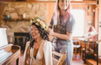A woman smiles at you as she has her wedding hairstyle done with a flower crown