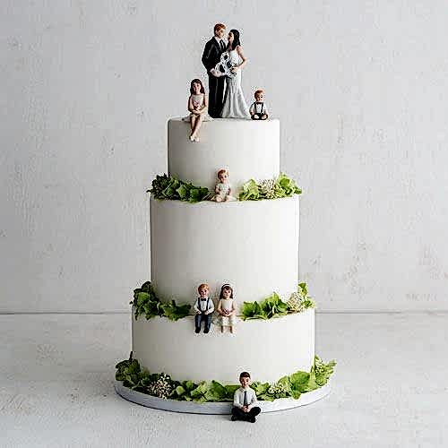 bride and groom holding ampersand cake topper with six children sitting on various tiers of the cake
