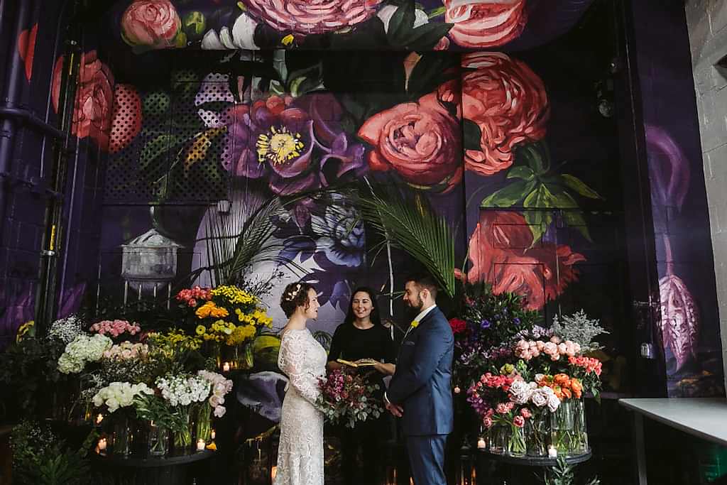 Couple reciting their wedding ceremony script in front a floral mural