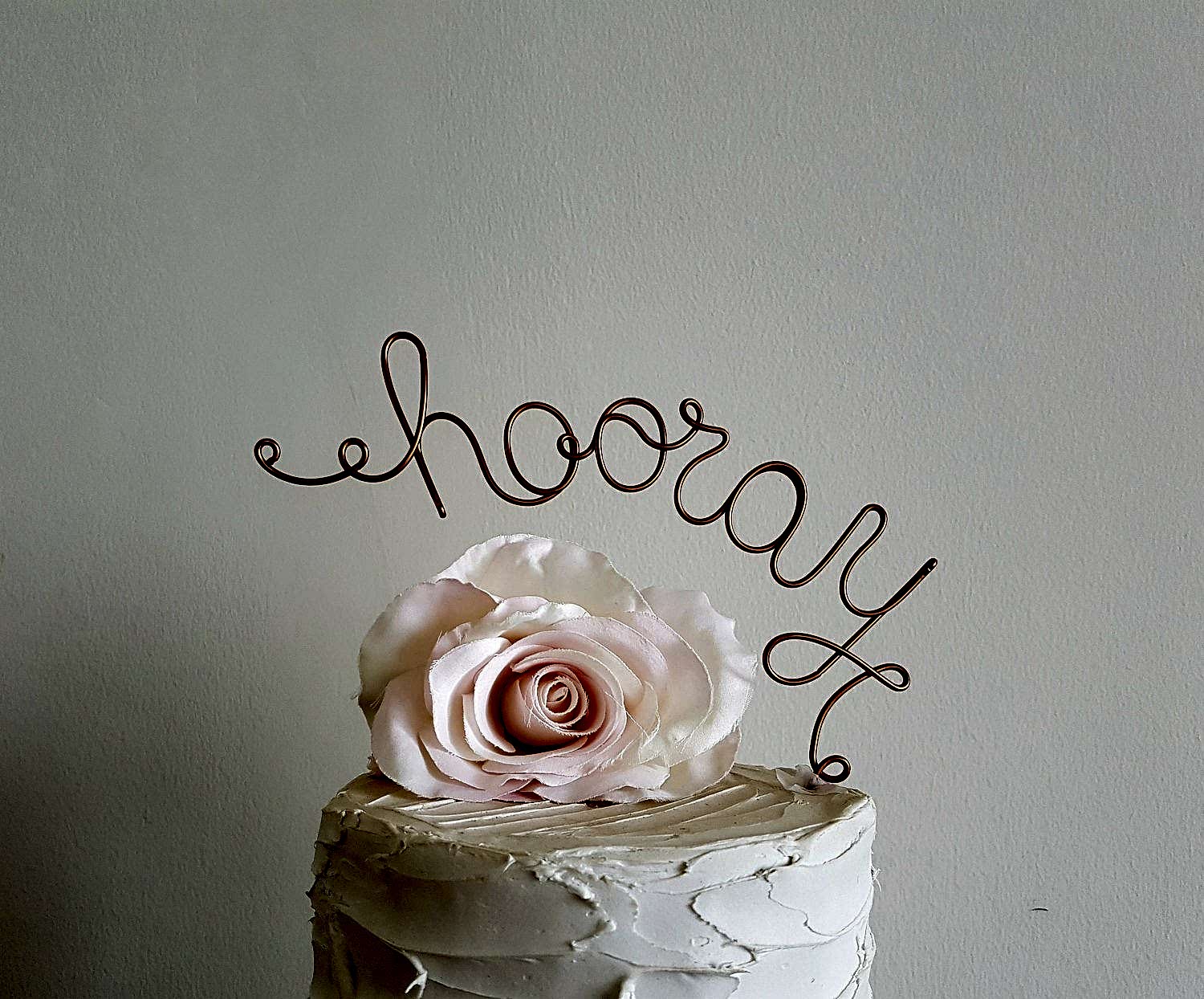copper wire that says "hooray" cake topper and a flower