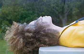 person in yellow laying down outside, with curly, kinky hair partially blocking face