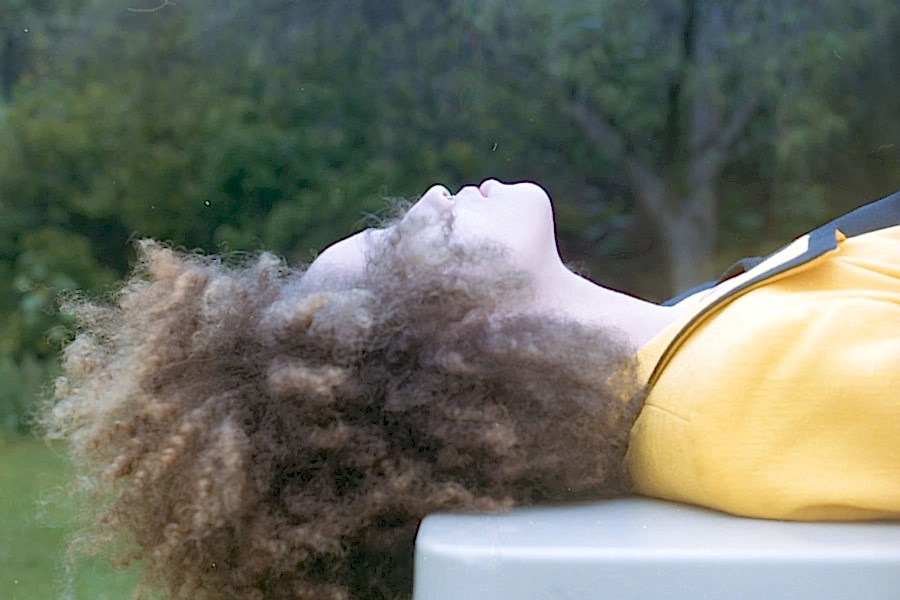 person in yellow laying down outside, with curly, kinky hair partially blocking face
