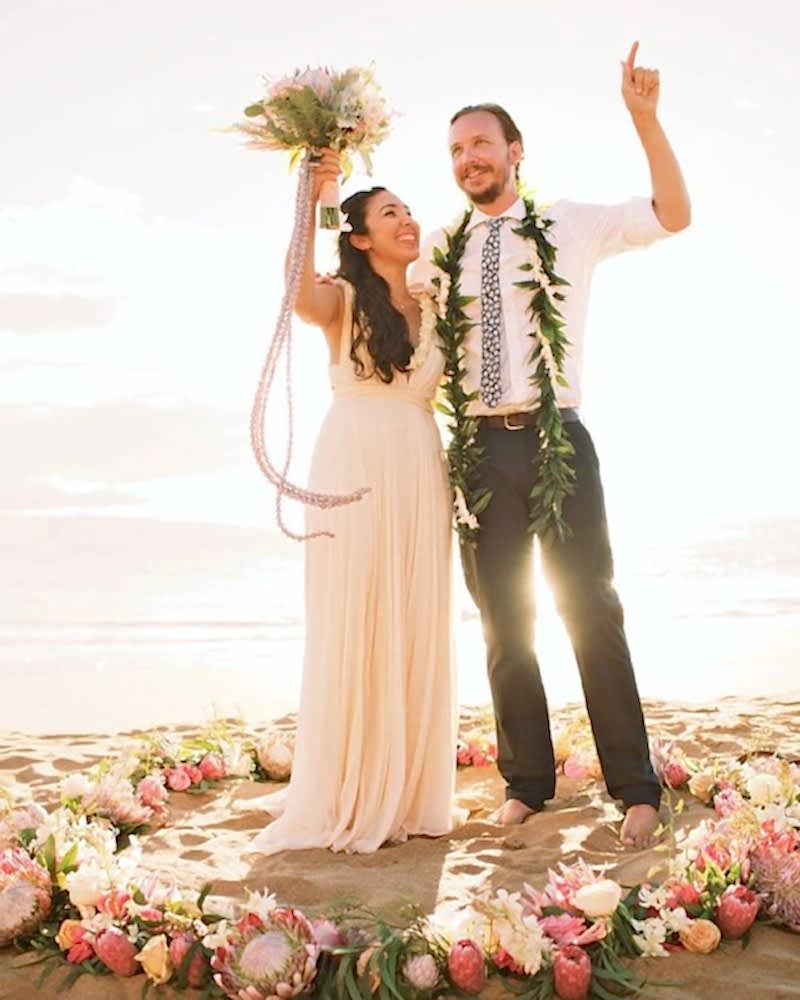 A couple stands with their hands in the air, at the beach
