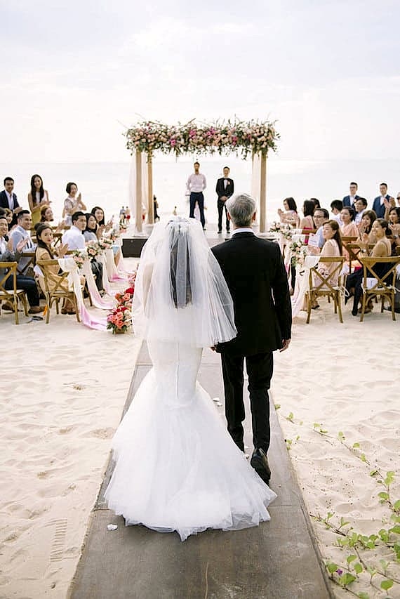 A bride walks toward her partner during a beach ceremony