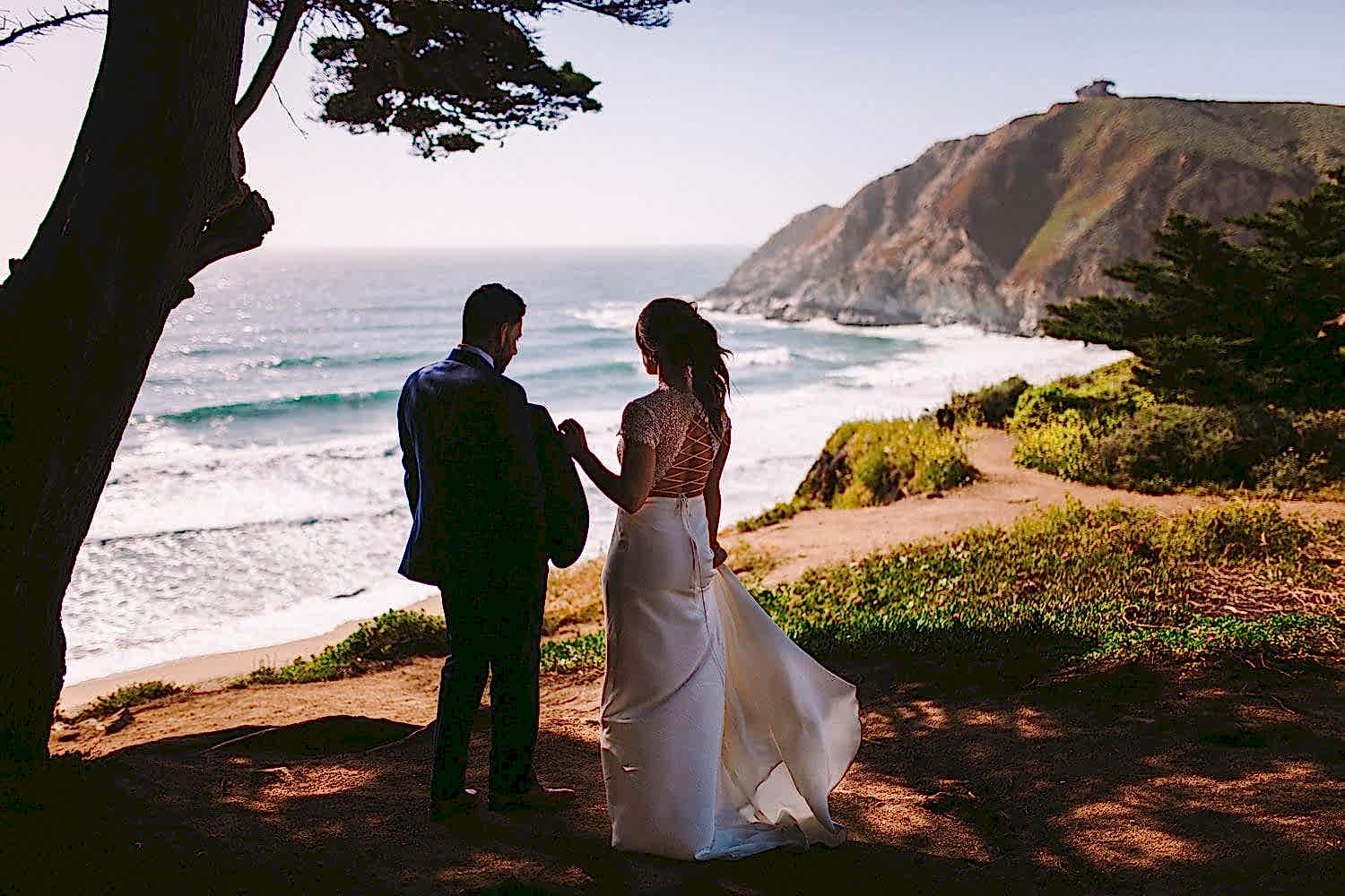 A man and woman stand on a hillside, overlooking the beach.