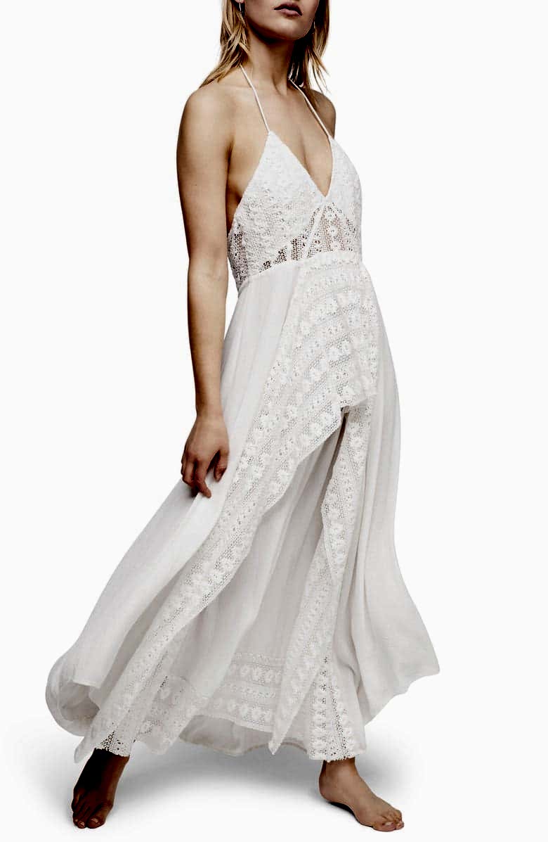 A woman wears a white dress with spaghetti strap halter, plunging v-neck, crocheted lace accents, and flowing skirt