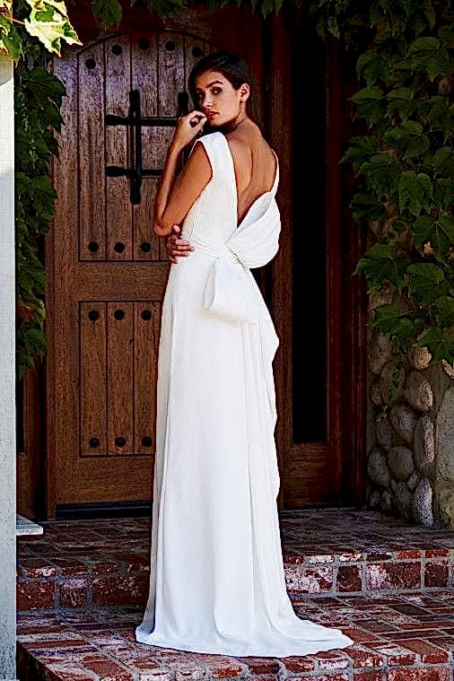 A woman wears a white dress with a large bow in the back