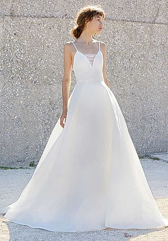 A woman wears a white dress with a triangle top bodice with spaghetti straps and a lace "modesty panel" across the plunge with a full a-line skirt