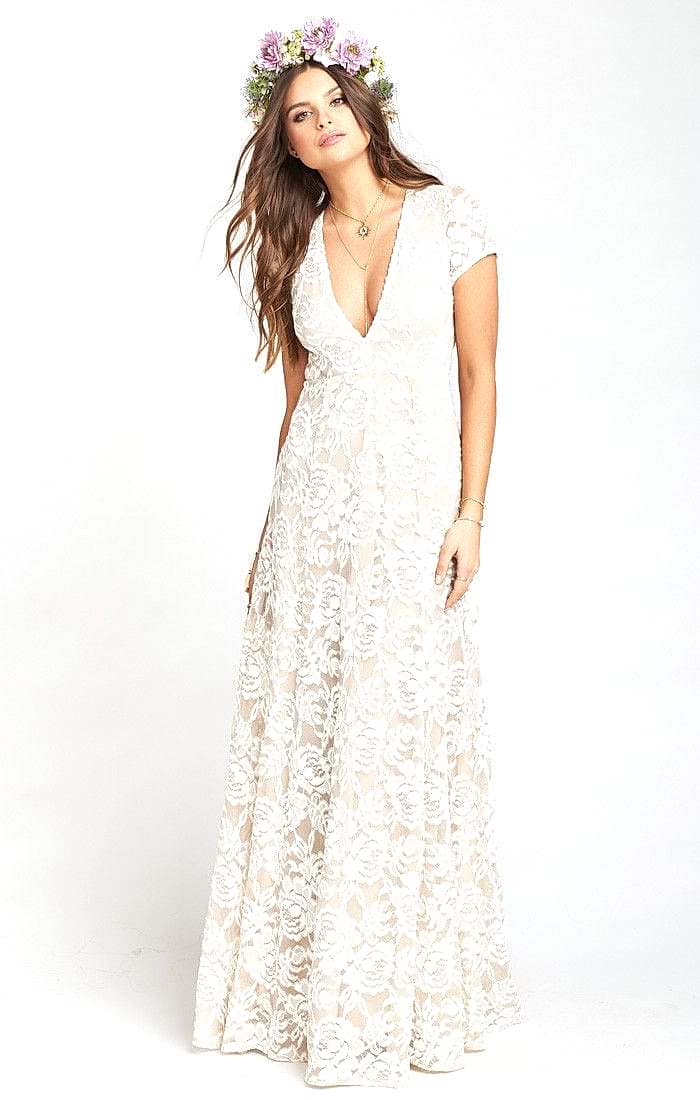A woman wears a white lace dress with a deep v-neck, short sleeves, and a large floral lace motif
