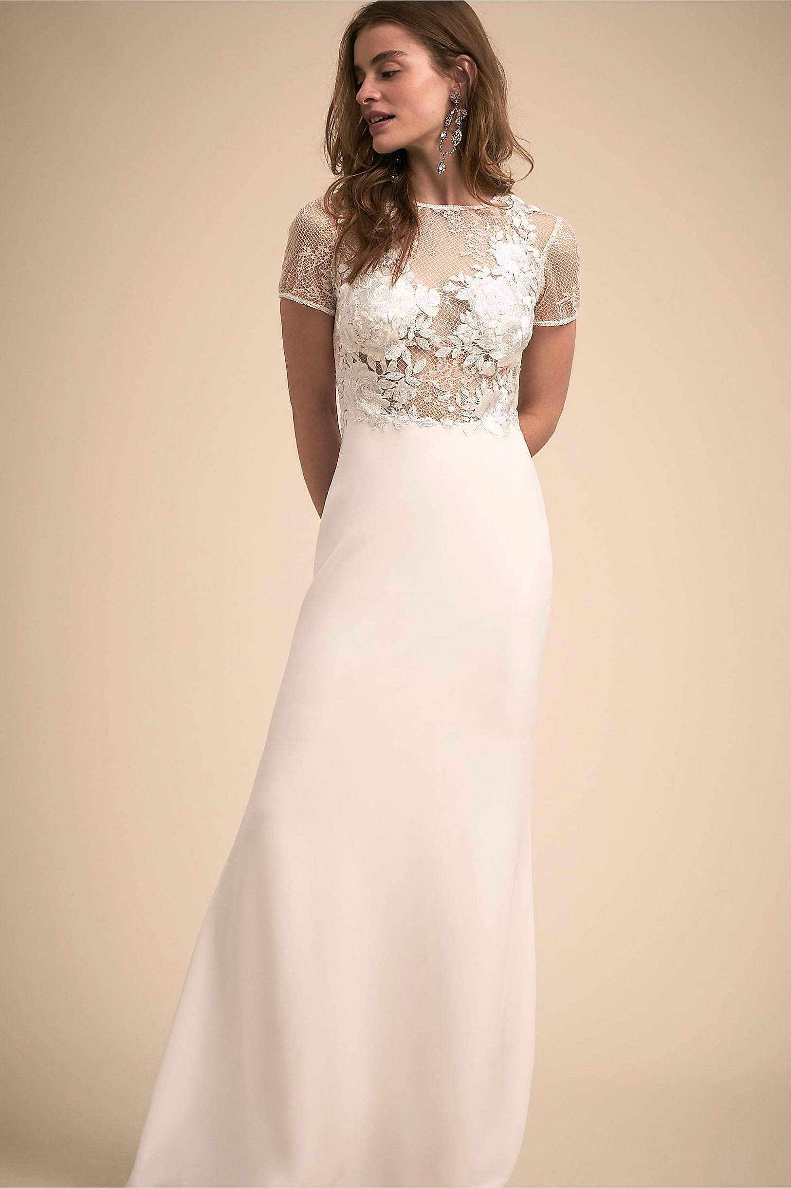 A woman wears an off-white dress with a sheer embroidered bodice with high neckline and short sleeves