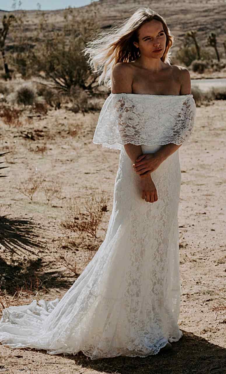 A woman wears a white lace dress with a low off-the-shoulder cut and a ruffle bodice