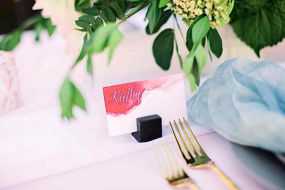 a close shot of a watercolor-style oxblood place card that reads "Kathy" in white calligraphy