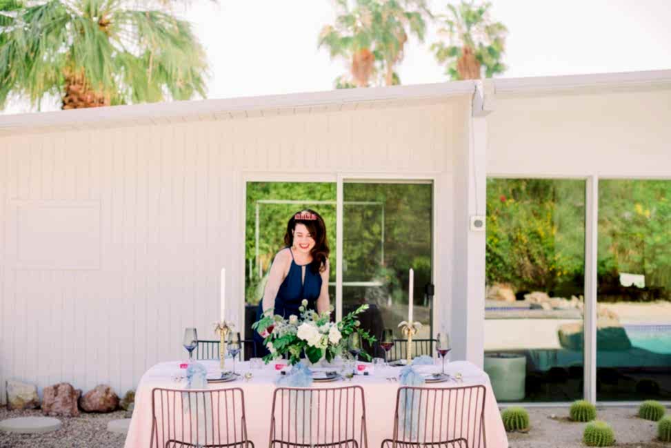 a woman in a sundress and tiara prepares a dinner table outdoors